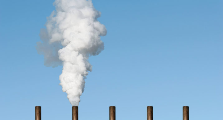 Line of chimney tops against blue sky with smoke emerging from one